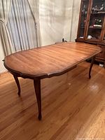 Wooden dining table seating six with carved legs and middle leaf expansion inserted, shown in wooden floor room.