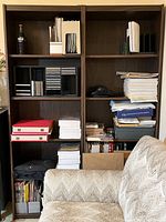 Front view of left side bookshelf filled with various items including books, binders, papers, and folders.