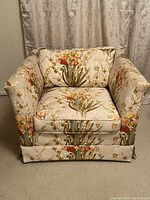 Front view of a floral upholstered lounge chair with orange and beige flowers on a light background showing cushioned seat, back and armrests.