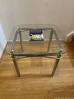 Glass side table with a bridge-themed book placed on top, showing the design and materials of the table.