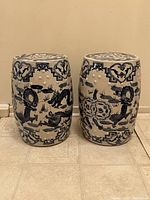 Two drum-shaped blue and white porcelain garden stools side by side, showing dragon and fretwork decoration on the sides.