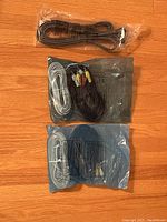 Three sealed bags of different cables arranged on a wooden floor, showing packaging and cable types.