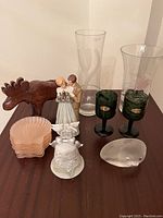 Photo showing wooden moose puzzle, two clear glass vases, two green goblets, 25th anniversary bell, figurine of a couple, pink shell shaped dishes, and clear glass sea life paperweight arranged on a wooden surface.