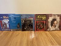 Photo of five LP albums standing upright against a wall, featuring various cover arts including a performer, Christmas theme, and a classical portrait.