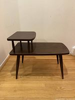 Wooden side table with an elevated smaller shelf to one side, four tapered legs, and a dark brown finish.