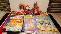 Collection of vintage children's books stacked together with toys placed behind them. Includes visible covers like 1936 Story Book and Pink Panther comic.