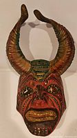 Front view of the carved Mexican carnival mask showing detailed facial carving, paintwork, and large curved horns.