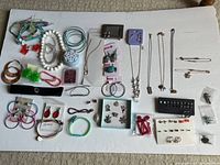Full assortment of costume jewelry including bracelets, earrings, necklaces, and rings laid out on white surface.