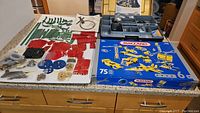 Loose vintage Meccano metal and plastic building pieces laid out with two kits in blue boxes.