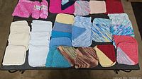 Full spread of 42 hand knit washcloths or dishcloths laid out on a table, showing variety of colors including white, cream, pink, blue, multicolor, and red shades.