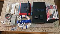 Full lot overview showing Nintendo Wii Mini with remotes, charging cables, sensor bar, Nerf racing wheel, Sony PS2 with Guitar Hero controller, memory cards, and stack of games