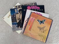 Eight vinyl records stacked on carpet showing front covers. Includes Heart signed album with butterfly cover, Jeff Healey and others visible.