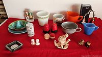 Full lot on red cloth including ceramics, glassware, figurines, shakers, and collectibles with variety of colors and styles