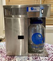 Front view of stainless steel distiller unit with glass collection jar in place