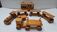 Four-piece wooden train set including the locomotive, three cars, and vintage cable car placed on white background.