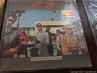 Photo of AC/DC 'Dirty Deeds Done Dirt Cheap' album cover with band members and title visible.