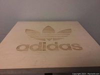 Close-up of the wooden table top showing the Adidas logo engraved in the center.