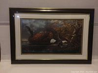 Photo of framed art showing two flying bald eagles over a river with fall foliage, wooden frame with gold trim.