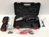 Mini chainsaw placed in open black plastic carrying case, with two batteries, red tool kit in plastic bag, gloves, and manual displayed around it.