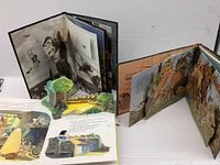 All 3 vintage pop-up books opened showing detailed 3D paper pop-up scenes including a dinosaur and biplanes.