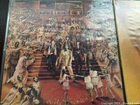 Photo of album cover with multiple figures on steps artwork, records in sleeves.