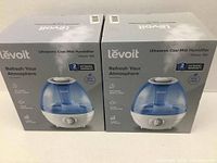 Two boxed Levoit Classic 100 Ultrasonic Cool Mist Humidifiers showing front packaging with product image and warranty info.