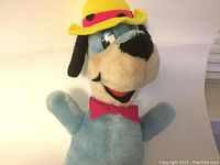 Front view of vintage Huckleberry Hound stuffed toy showing facial features, yellow hat with red band, and red bow tie.