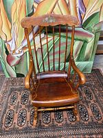Full front view of antique wooden rocking chair showing floral detail on backrest and seat shape.