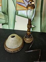 View of lamp base with intricate bronze-colored metalwork, amber glass globe, clear tornado-shaped glass section, and detached frosted glass etched shade dome.
