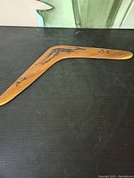 Full view of wooden boomerang with Aboriginal art on black surface