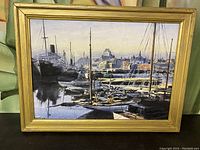 Framed oil on canvas painting showing harbor with boats and buildings in the background.