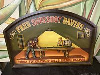 Full view of the wooden billiards sign showing the arched top, the painted background with 3D figurines of billiards players and pool table, advertising Fred "Sureshot" Davies.