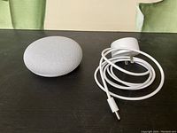 Google Home Mini speaker beside white power adapter and cable on dark surface