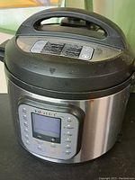Full view of Instant Pot including lid and handle with external stainless steel casing and dust/debris on top surface.