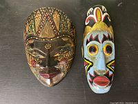 Two painted masks shown side by side on a dark surface