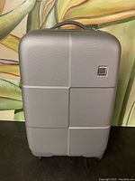 Full front view of grey hard shell suitcase with Olympia logo plaque.