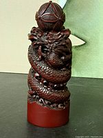 Front view of the wooden dragon coiled around a spherical ornament on a cylindrical base, showcasing detailed scales and facial features.