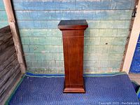 Full front view of the wooden pedestal showing its height and paneled body.