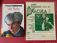 Both items displayed flat on red background: the green and white Dracula film sheet at right and the Andy Warhol biography at left.