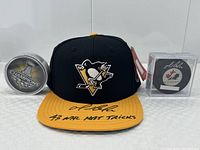 Front view of black and yellow Pittsburgh Penguins hat centered between two hockey pucks