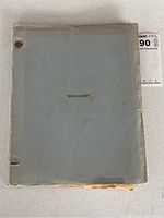 Grey cardstock bound cover of script showing two-hole punch binding at top and bottom left, surface creases and edge wear