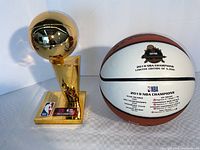 Front view of gold-tone replica trophy next to white-panel commemorative basketball