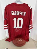 Full lot showing red Garoppolo jersey hung on hanger with autographed football below