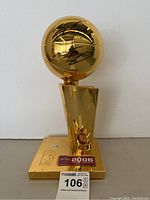 Full view of gold-tone NBA championship trophy replica with base plaque reading '2006 NBA Champions'. Front shows two autographs on basketball section.