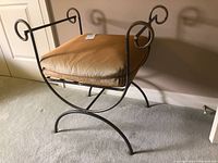 Side view of metal frame chair with brown cushion, showing curved scroll arm design and wear to metal finish.