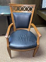 Front view of the wood base chair showing black leather seat and back, nailhead trim detail, and curved armrests.