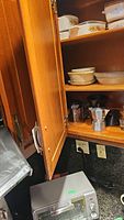 Photo of wooden kitchen cabinet shelves with Corning Ware dishes, espresso coffee pot, and dessert bowls.