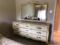 Front view of nine drawer cream dresser with matching large decorative mirror hung above it