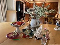 Wide view of all figurines and decor including candy dish, faux fruit bowl, jug with flowers, and porcelain and glass figurines.