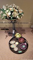 Full view of the artificial floral arrangement on metal stand with a tray of assorted decorative bowls and dishes below.